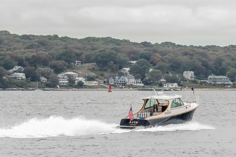 Slide: The Image of Hinckley Talaria 34 boat cruising on water near coastal homes, 2013 model. - 8