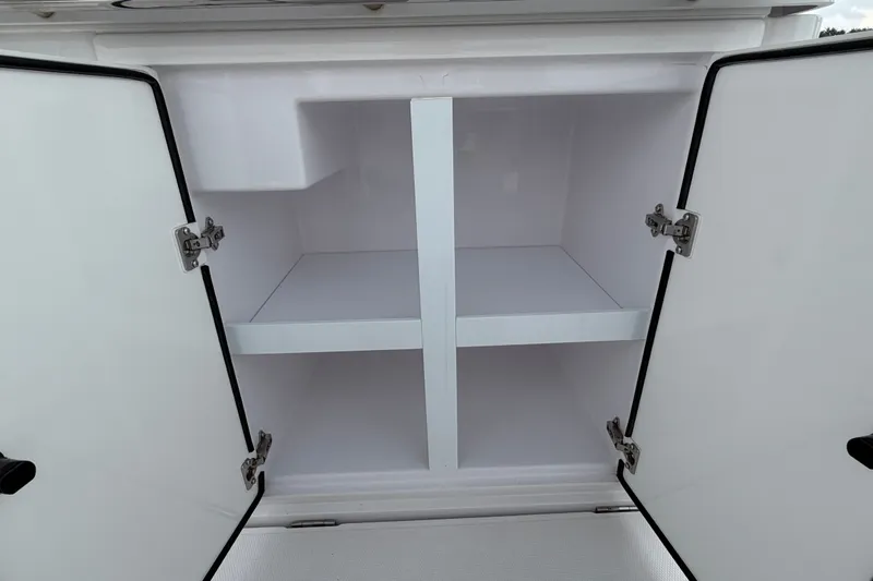 Slide: The Image of Open storage compartment on 2023 Axopar 28 Cabin boat, featuring white interior shelves. - 43