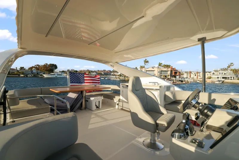 Slide: The Image of Das Bild zeigt das Cockpit einer Absolute Navetta 48 von 2020 mit einem eleganten Steuerstand und einem Tisch. Im Hintergrund sind Wasser und Häuser zu sehen. - 12
