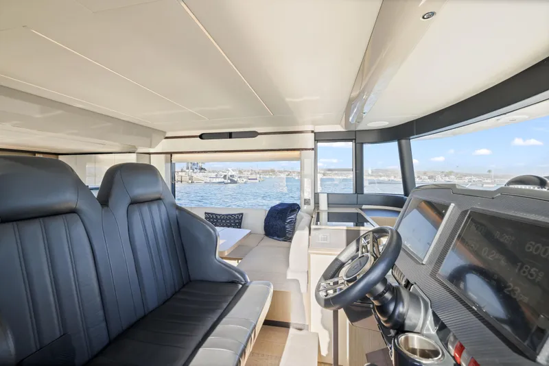 Slide: The Image of Das Innere einer Absolute Navetta 48 von 2020 zeigt ein modernes Cockpit mit Ledersitzen und einem Steuerstand. Große Fenster bieten einen Blick auf das Wasser. - 25