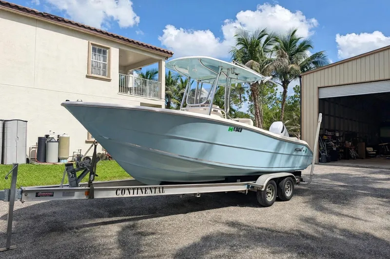 Slide: The Image of 2021 Bulls Bay 230 Center Console boat on trailer, parked near a garage and palm trees. - 17