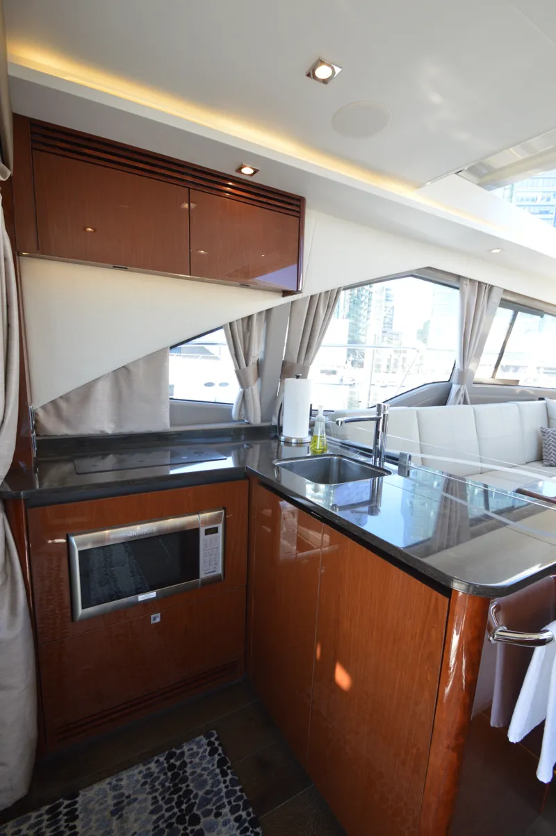 Slide: The Image of The interior of a 2018 Sea Ray 460 Express Cruiser features a modern kitchen with wood cabinets and a microwave. - 27