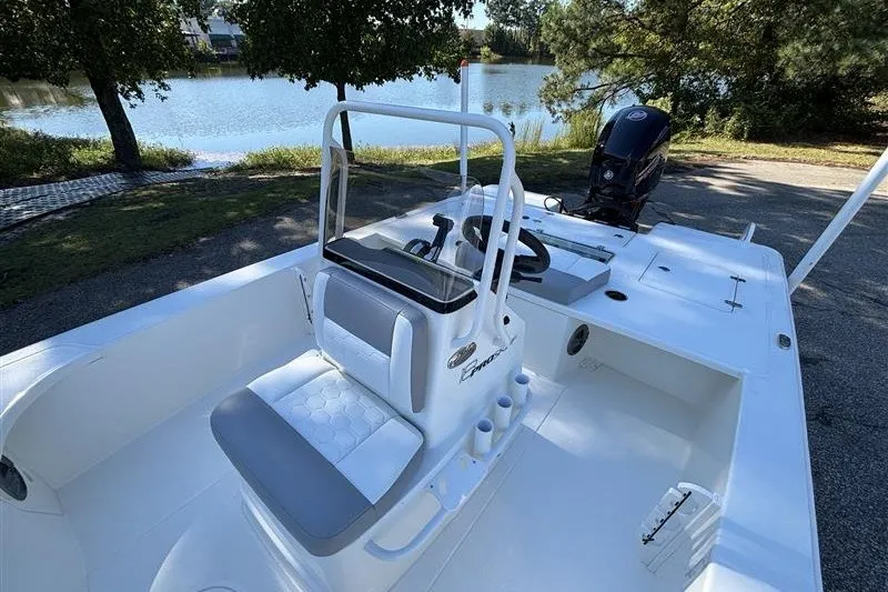 Slide: The Image of 2026 Mako 18 Pro Skiff boat with seating, steering console, and outboard motor by a lake. - 15