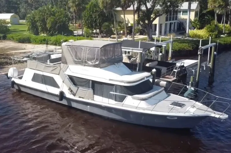 The Image of 1987 Bluewater Yachts Coastal Cruiser 51 docked by lush greenery and waterfront homes. - 0
