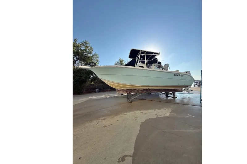 The Image of 2004 Sea Fox 257 Center Console on a trailer, with blue canopy, parked outdoors. - 0