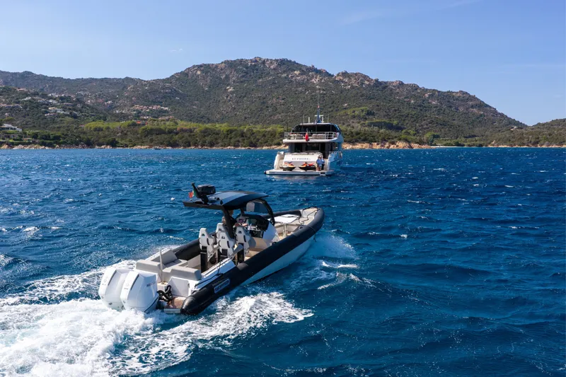Slide: The Image of A sleek 2025 Alpha 100 Squalo boat cruising on a vibrant blue sea near a mountainous coastline. - 17