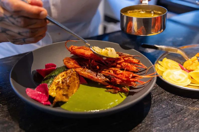 Slide: The Image of Chef preparing gourmet shrimp dish with vibrant sauce and vegetables on a dark plate. - 20