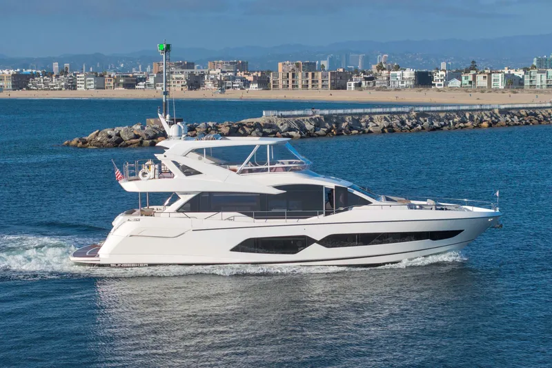 Slide: The Image of 2018 Sunseeker 76 Yacht cruising near a coastal city with modern buildings. - 10