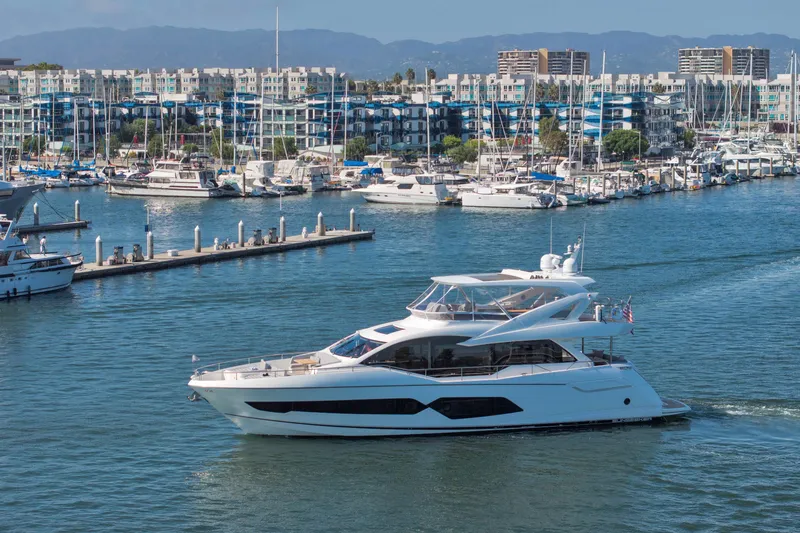 Slide: The Image of 2018 Sunseeker 76 Yacht cruising in a marina with modern buildings in the background. - 1