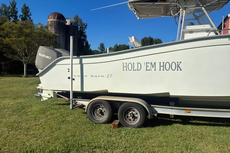 Slide: The Image of Cape Horn 27XS boat on trailer, named "Hold 'Em Hook," with Suzuki engine, parked on grass. - 16