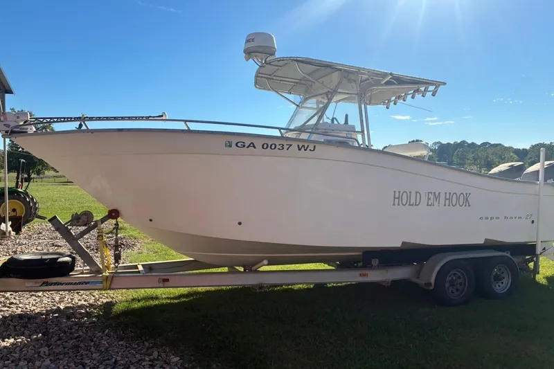 Slide: The Image of 2000 Cape Horn 27XS boat named "Hold 'Em Hook" on a trailer in sunny yard. - 2