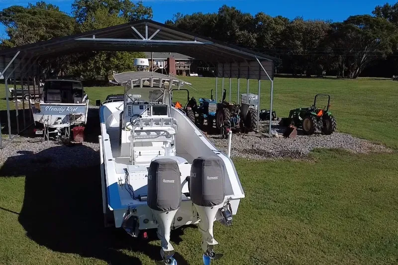 Slide: The Image of 2000 Cape Horn 27XS boat with dual engines, parked under a metal shelter on grassy terrain. - 13