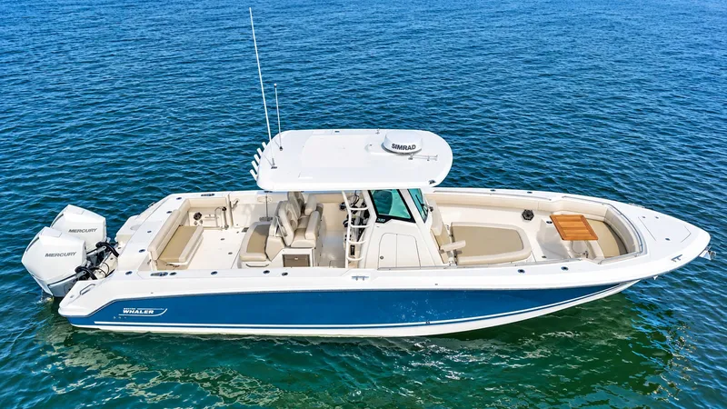 Slide: The Image of A 2024 Boston Whaler 330 Outrage on calm water. It features a blue and white design with twin outboard engines. - 9