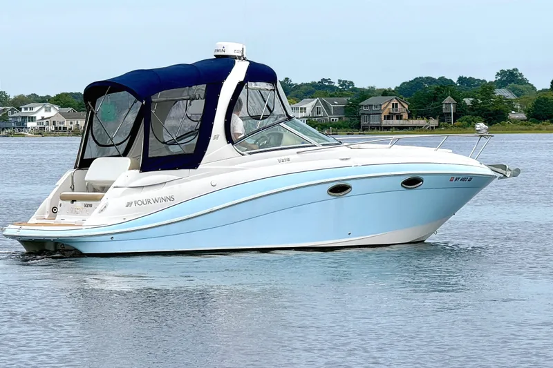 The Image of 2009 Four Winns 278 Vista boat with blue hull, cruising on calm water near shoreline homes. - 0