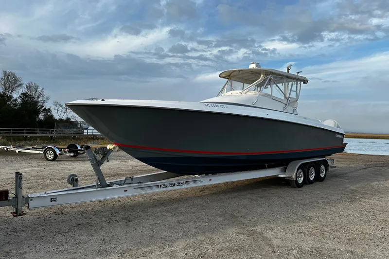 Slide: The Image of 2006 Contender 36 Fisharound boat on trailer, parked near water under cloudy sky. - 0