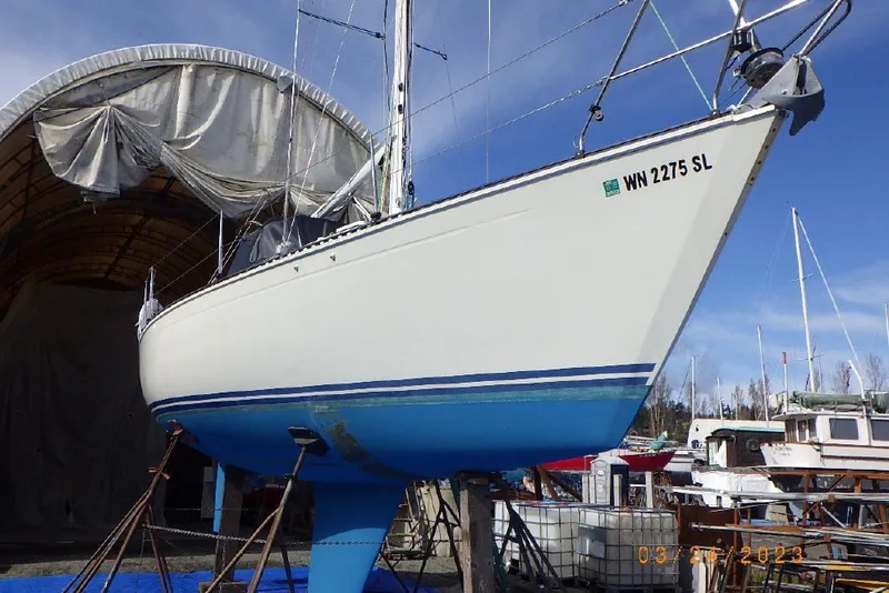 Slide: The Image of 1989 C&C 30 MKII sailboat on stands, with blue hull and white deck, in a boatyard. - 90
