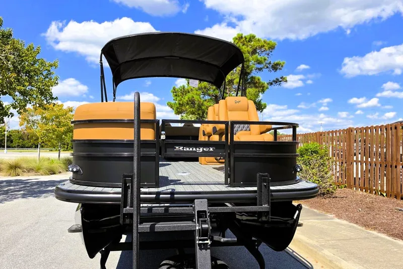 Slide: The Image of 2027 Ranger 220FC pontoon boat with tan seating, parked outdoors under a blue sky. - 10