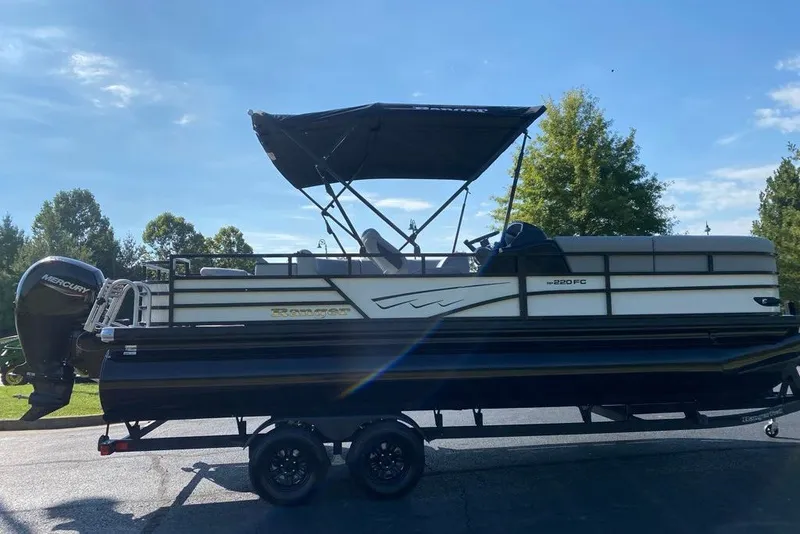 Slide: The Image of 2027 Ranger 220FC pontoon boat with Mercury engine on trailer, parked outdoors. - 1