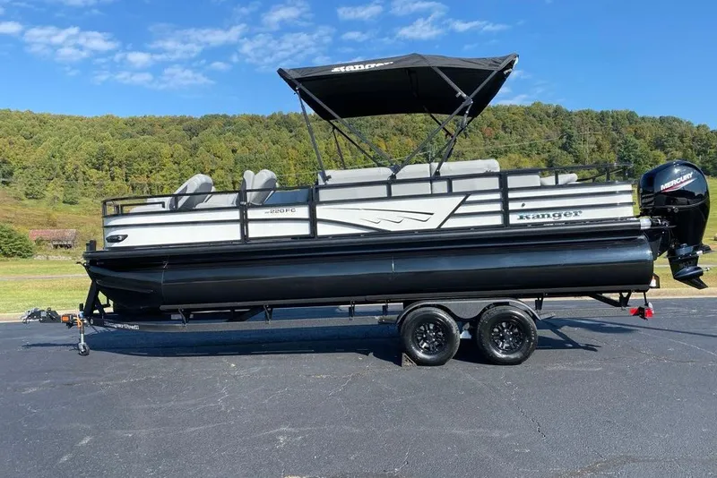 Slide: The Image of 2027 Ranger 220FC pontoon boat on trailer, parked outdoors with scenic background. - 7