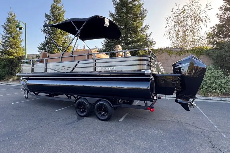Slide: The Image of 2027 Ranger 223F pontoon boat on trailer, parked in a lot with trees in the background. - 2