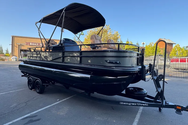 Slide: The Image of 2027 Ranger 223F pontoon boat on trailer, parked outdoors near a boat store. - 4