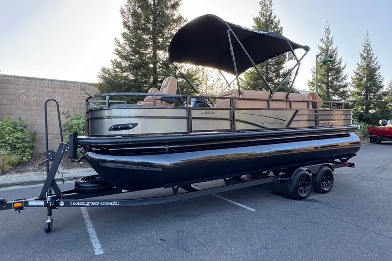 Slide: The Image of 2027 Ranger 223F pontoon boat on trailer, parked outdoors with canopy and seating. - 3