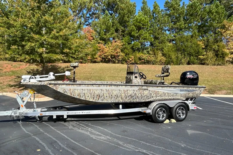 Slide: The Image of 2027 Ranger RB200 boat on trailer, camo design, parked outdoors with trees in background. - 2