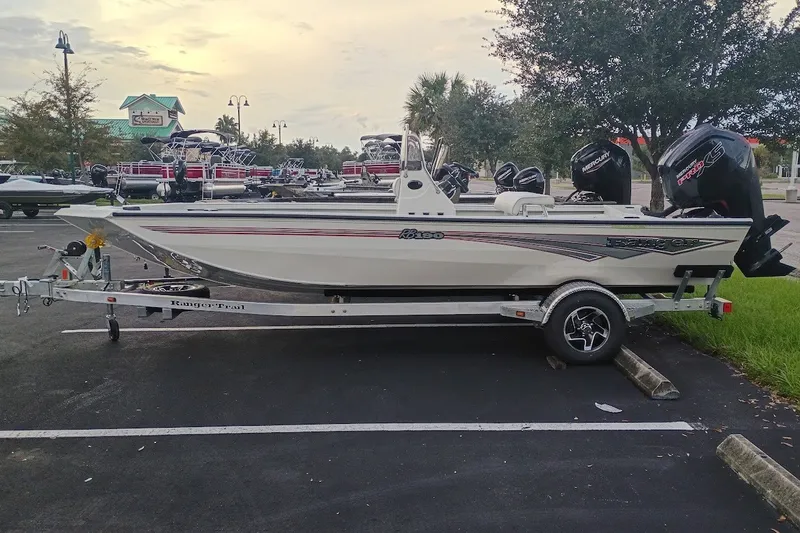 Slide: The Image of 2027 Ranger RB190 boat on trailer in parking lot, surrounded by trees and other boats. - 2