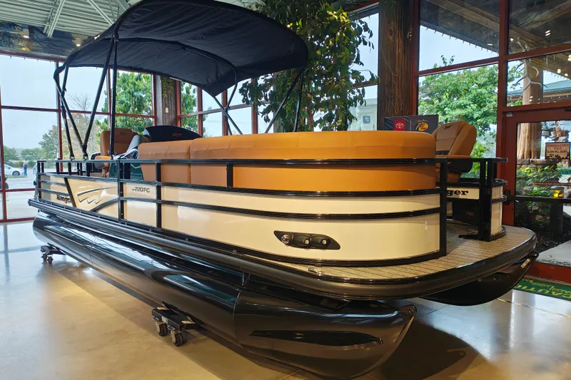 Slide: The Image of 2027 Ranger 220FC pontoon boat with tan seating and black canopy in showroom. - 1