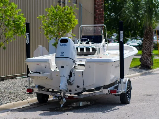 Slide: The Image of A white Bulls Bay 2000 boat on a trailer, parked beside a building with trees. - 4
