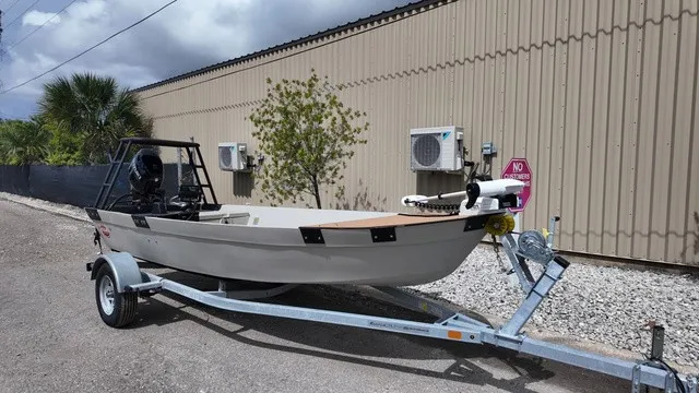 The Image of A 2024 gray shallow water skiff on a trailer, parked beside a building. - 0