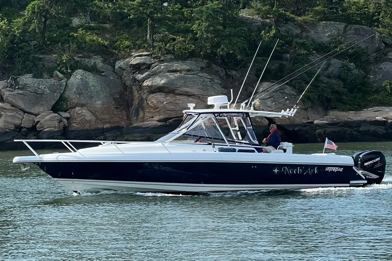 Slide: The Image of 2001 Intrepid 348 Walkaround boat cruising near rocky shoreline with lush greenery. - 2