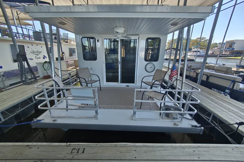 Slide: The Image of 2023 Catamaran Cruisers 1245 houseboat docked, featuring a cozy deck with chairs and railing. - 8