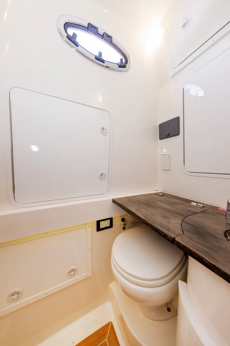 Slide: The Image of The image shows a clean boat toilet with a round window and a wooden shelf. - 40