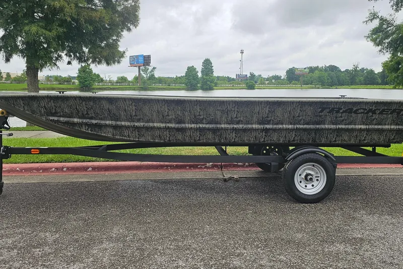 The Image of 2027 Tracker Grizzly 1648 Utility boat on trailer by a lake, overcast sky. - 0