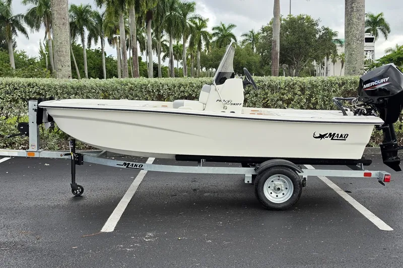 Slide: The Image of 2026 Mako Pro Skiff 13 CC boat on trailer, parked outdoors with palm trees. - 1