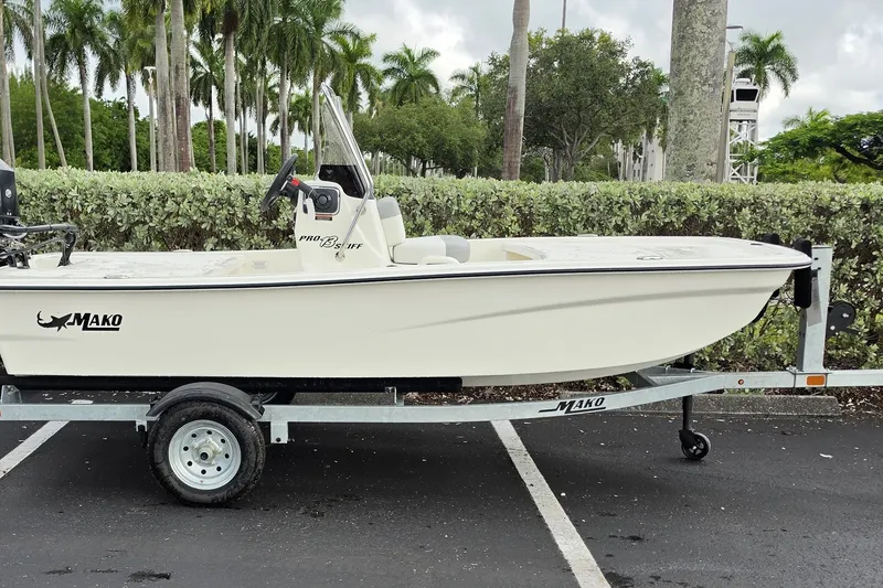 Slide: The Image of 2026 Mako Pro Skiff 13 CC boat on trailer, parked outdoors with lush greenery. - 2