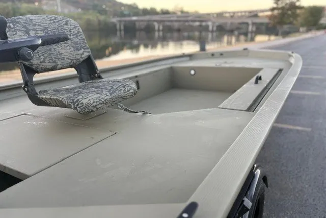 Slide: The Image of 2027 Tracker Grizzly 1654 T Sportsman boat with camo seat, parked near a serene river. - 15