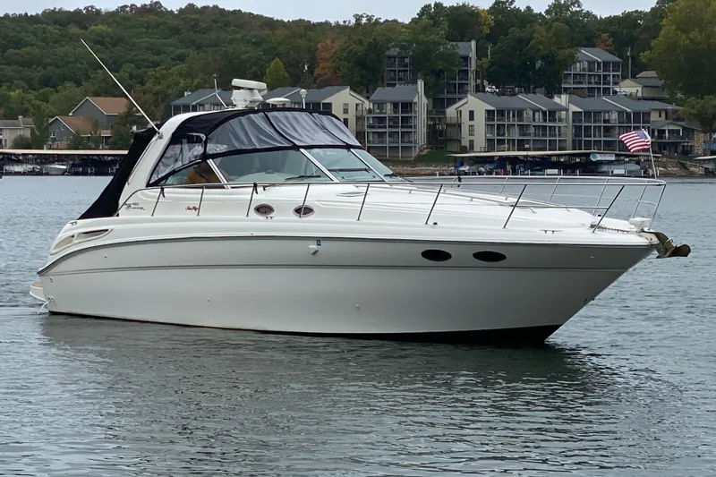 The Image of 1999 Sea Ray 380 Sundancer yacht on a lake with shoreline buildings in the background. - 1