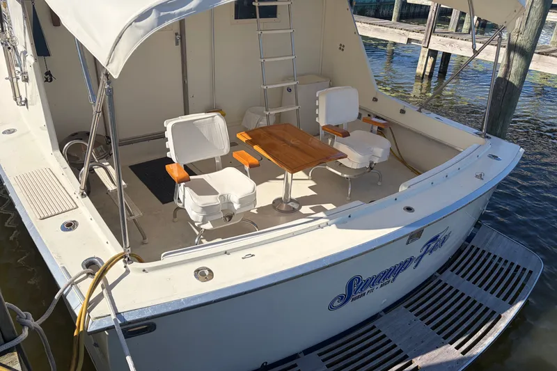 Slide: The Image of 1972 Hatteras 38 Convertible boat with seating and table on deck, docked by the water. - 6