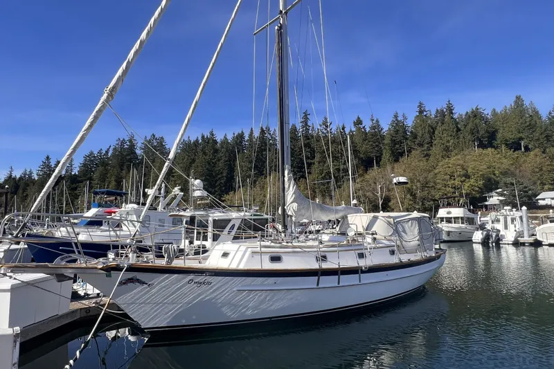 The Image of 1995 Cabo Rico 34 sailboat docked in a serene marina with forested background. - 0