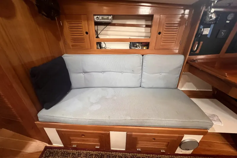 Slide: The Image of Cozy interior seating on a 1995 Cabo Rico 34 sailboat, featuring wooden cabinetry and blue cushions. - 54