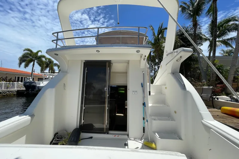 Slide: The Image of 2002 Silverton 330 Sport Bridge yacht docked, featuring open cabin and stairs, surrounded by palm trees. - 17