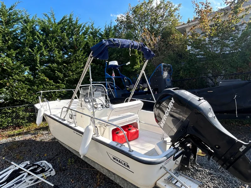 The Image of A 2007 Boston Whaler 17 Montauk on a gravel lot. It features an outboard motor and a Bimini top. - 0