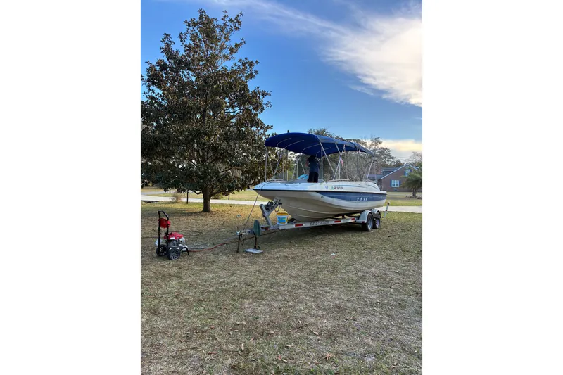 Slide: The Image of 2006 Bayliner 210 Classic boat on trailer with blue canopy, parked on grass. - 2