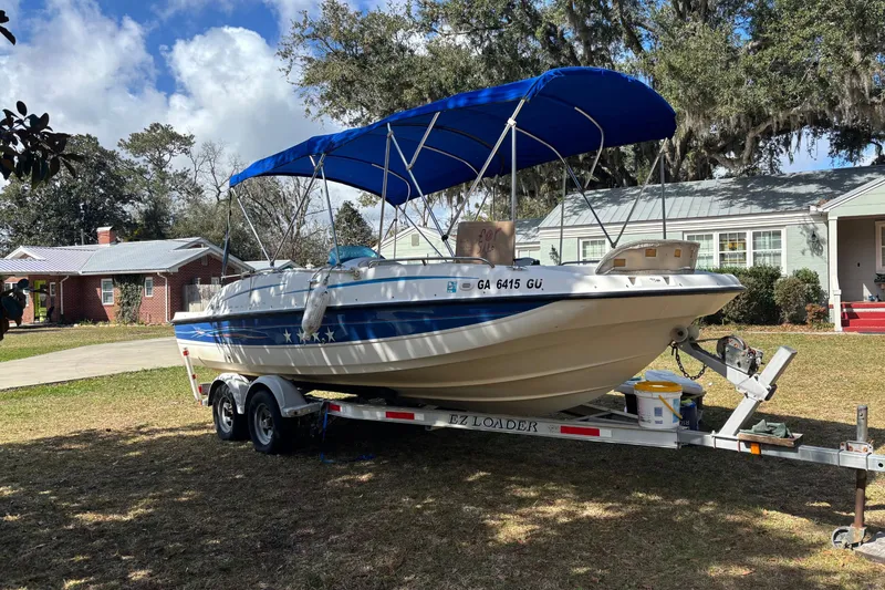 The Image of 2006 Bayliner 210 Classic boat on trailer with blue canopy, parked in residential yard. - 0