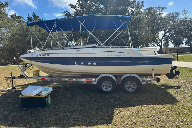 Slide: The Image of 2006 Bayliner 210 Classic boat on trailer with blue canopy, parked on grass. - 3