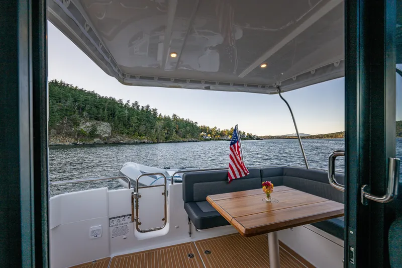 Slide: The Image of 2024 Nimbus 365 Coupe boat interior with lake view, American flag, and wooden table. - 23