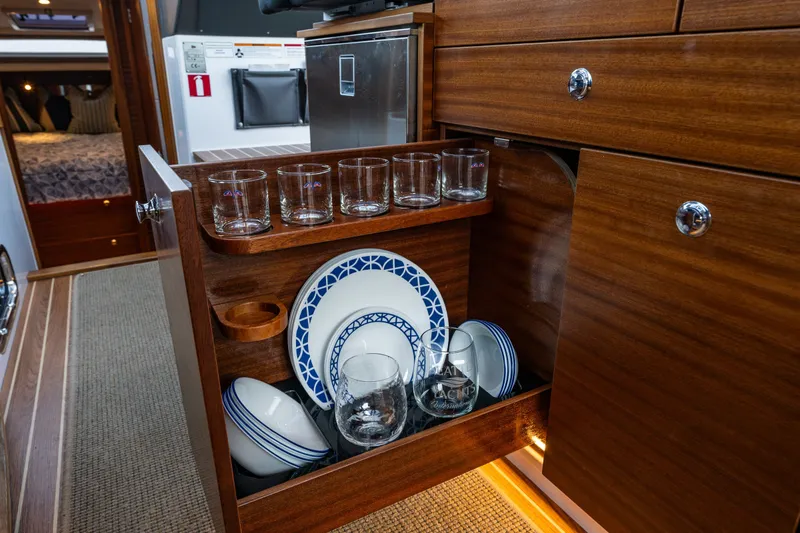 Slide: The Image of 2024 Nimbus 365 Coupe interior with wooden cabinetry, glassware, and plates neatly organized. - 11