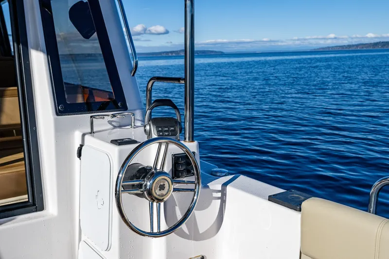 Slide: The Image of 2023 Ranger Tugs R-29 CB helm with ocean view, featuring steering wheel and controls. - 22